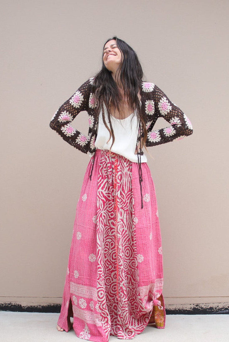 Woman in a floral top and pink patterned skirt standing in a room with a table and chairs.