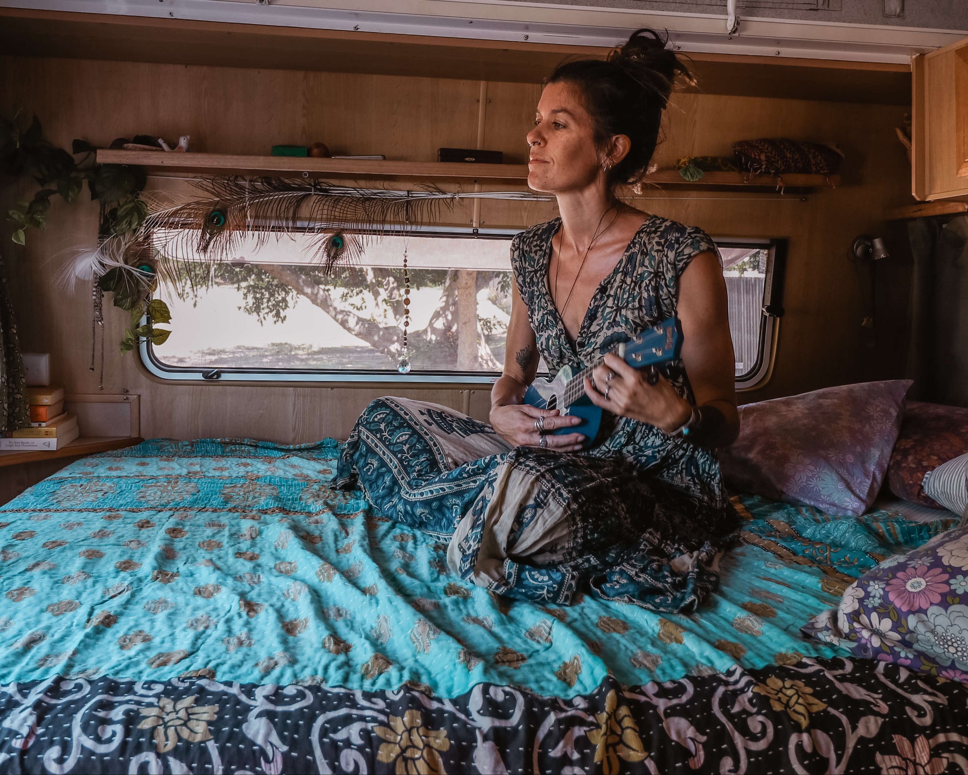 Woman sitting on a bed inside a camper van holding a guitar.
