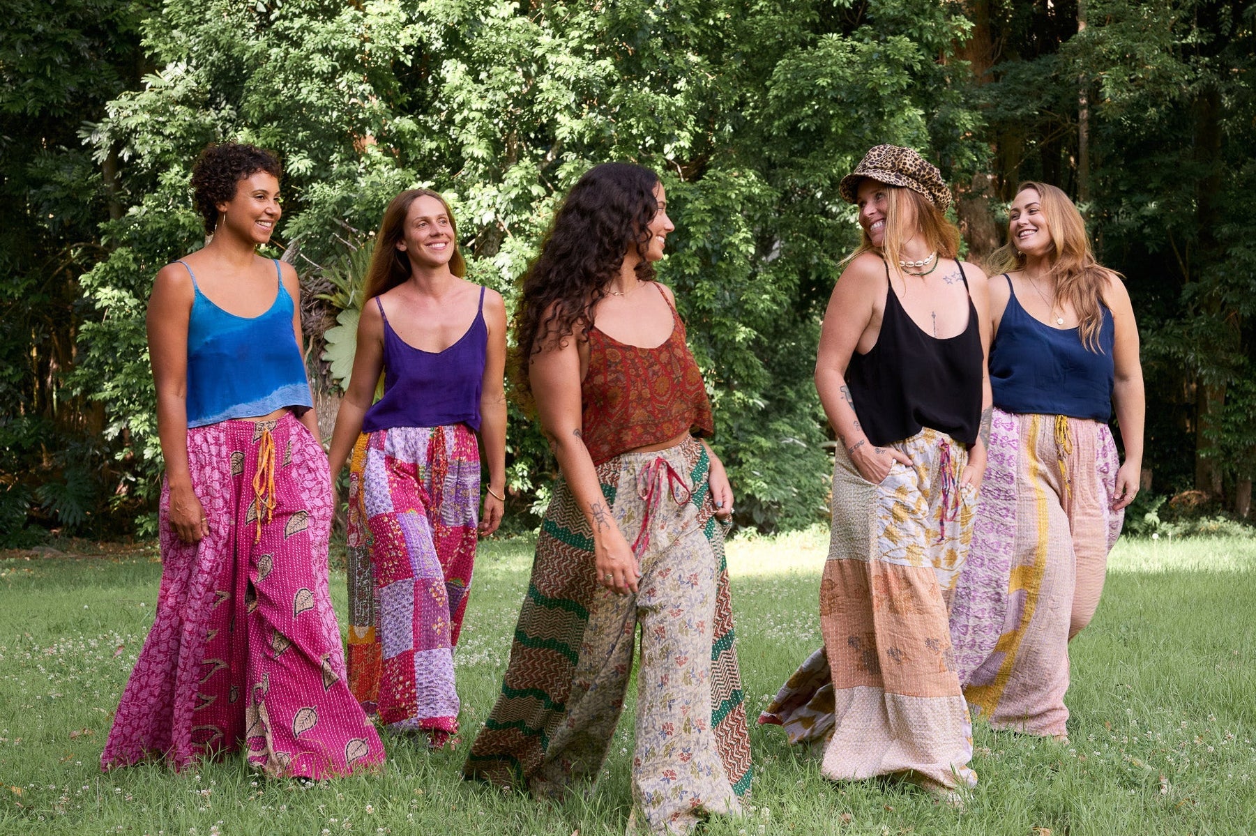 Five women in colorful outfits standing in a grassy area with trees in the background