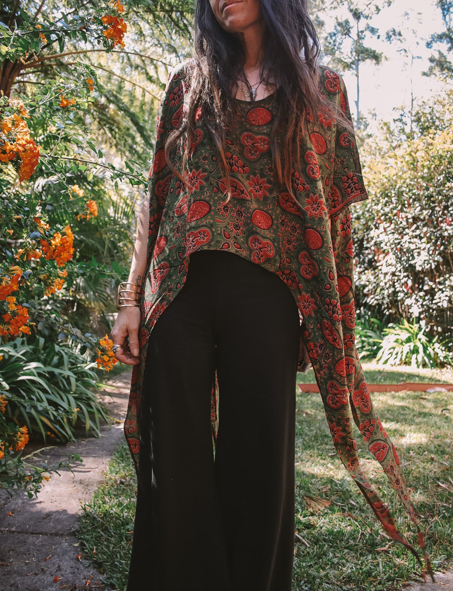 Person wearing a patterned top and black pants in a garden setting