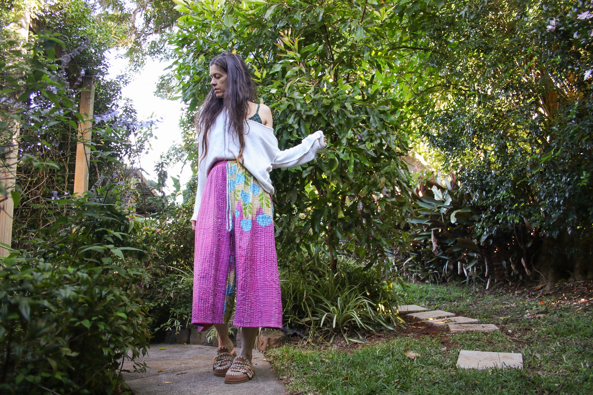 Woman walking outdoors in a garden with greenery wearing pink culottes