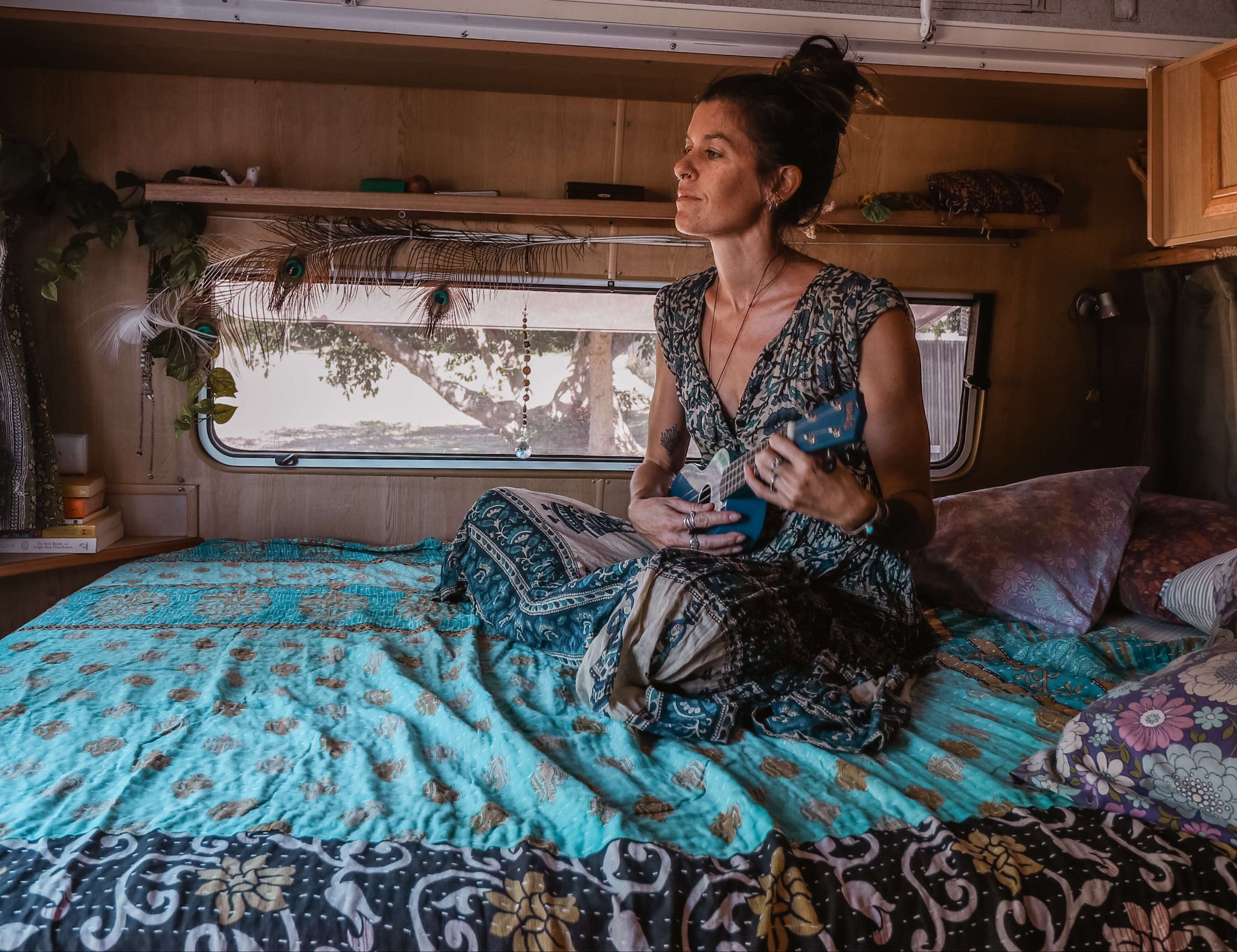 Woman sitting on a bed inside a camper van holding a guitar.