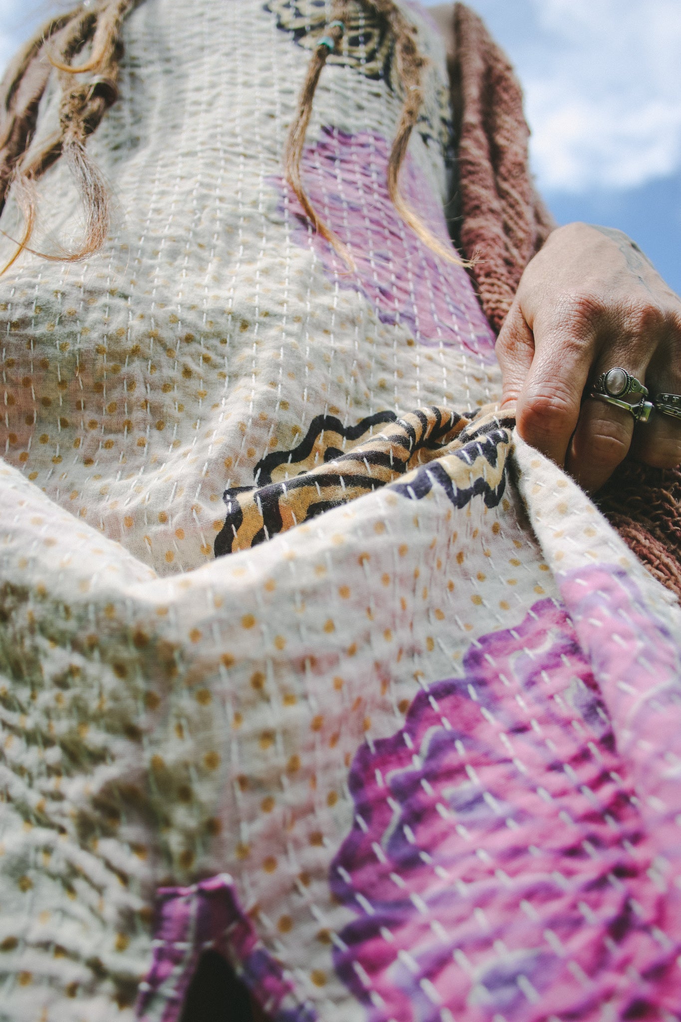 Close-up of a hand holding a textured fabric with floral patterns against a blue sky.