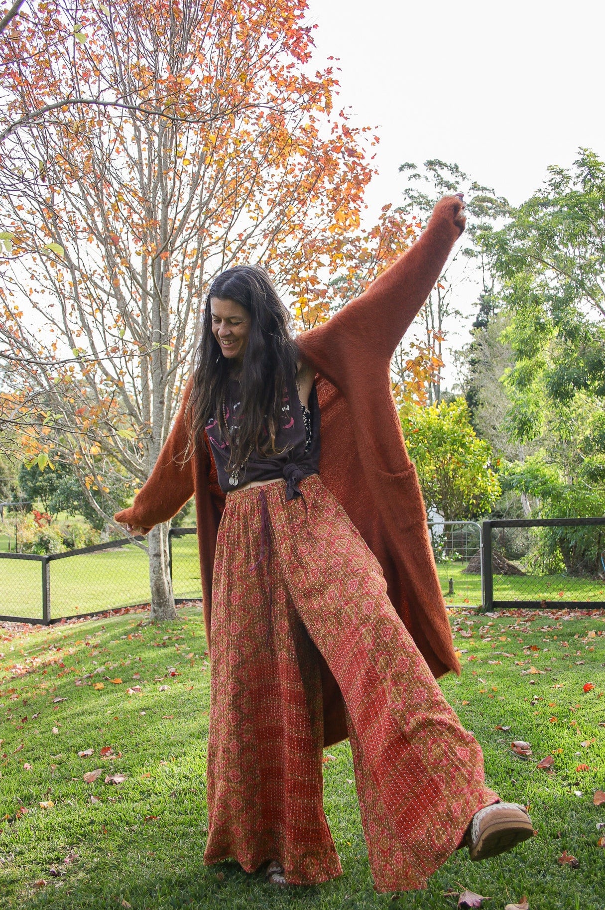 Woman in a long, patterned coat standing in a park with trees and grass in the background