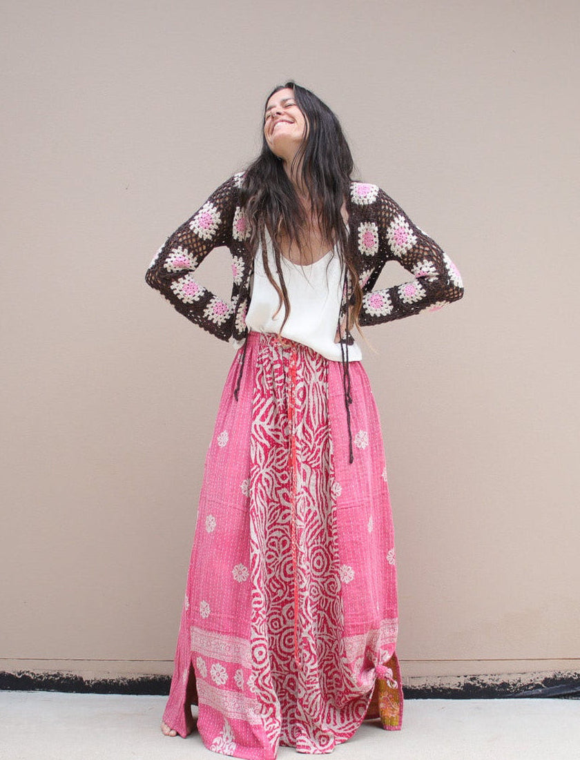 Woman in a floral top and pink patterned skirt standing in a room with a table and chairs.