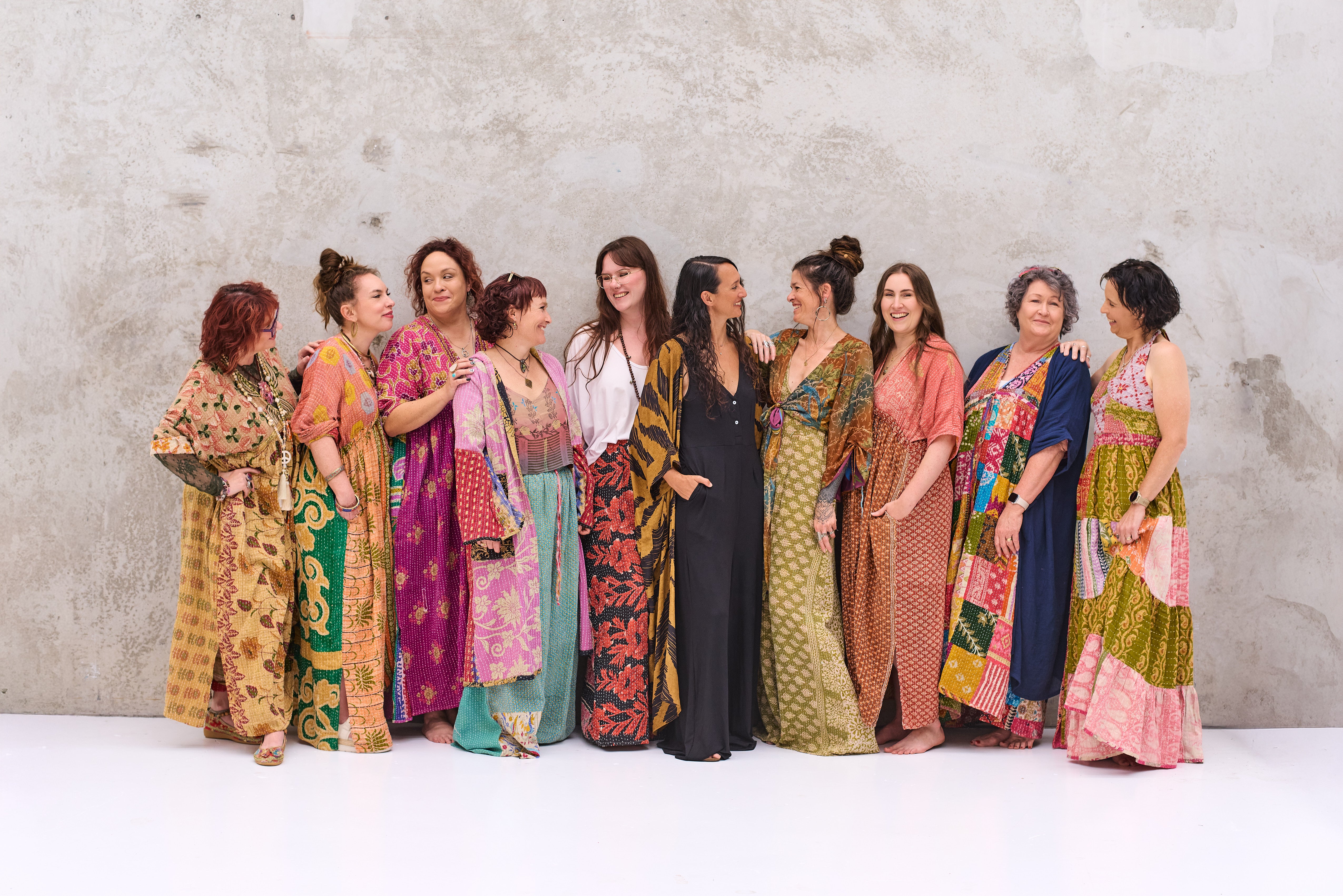 Group of women wearing colorful kantha outfits against a plain background