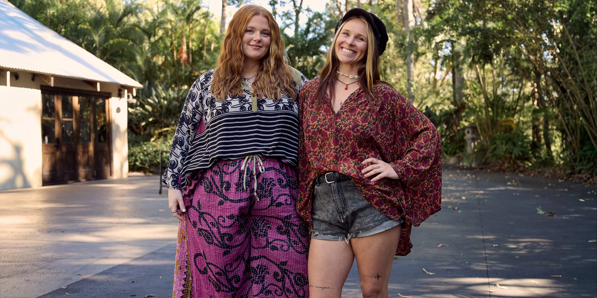 Two women standing outdoors in a natural setting, wearing patterned clothing.
