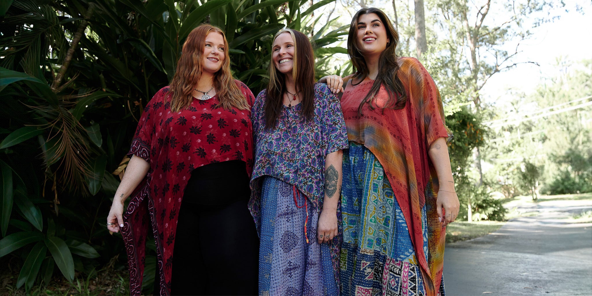 Three women standing together outdoors, wearing colorful and patterned clothing.