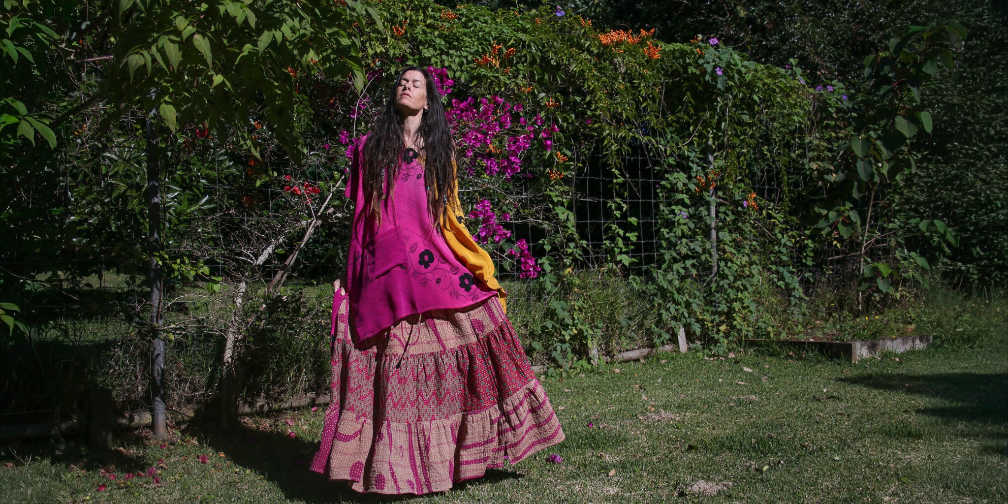 Woman in a pink dress standing in a garden with flowers and greenery.