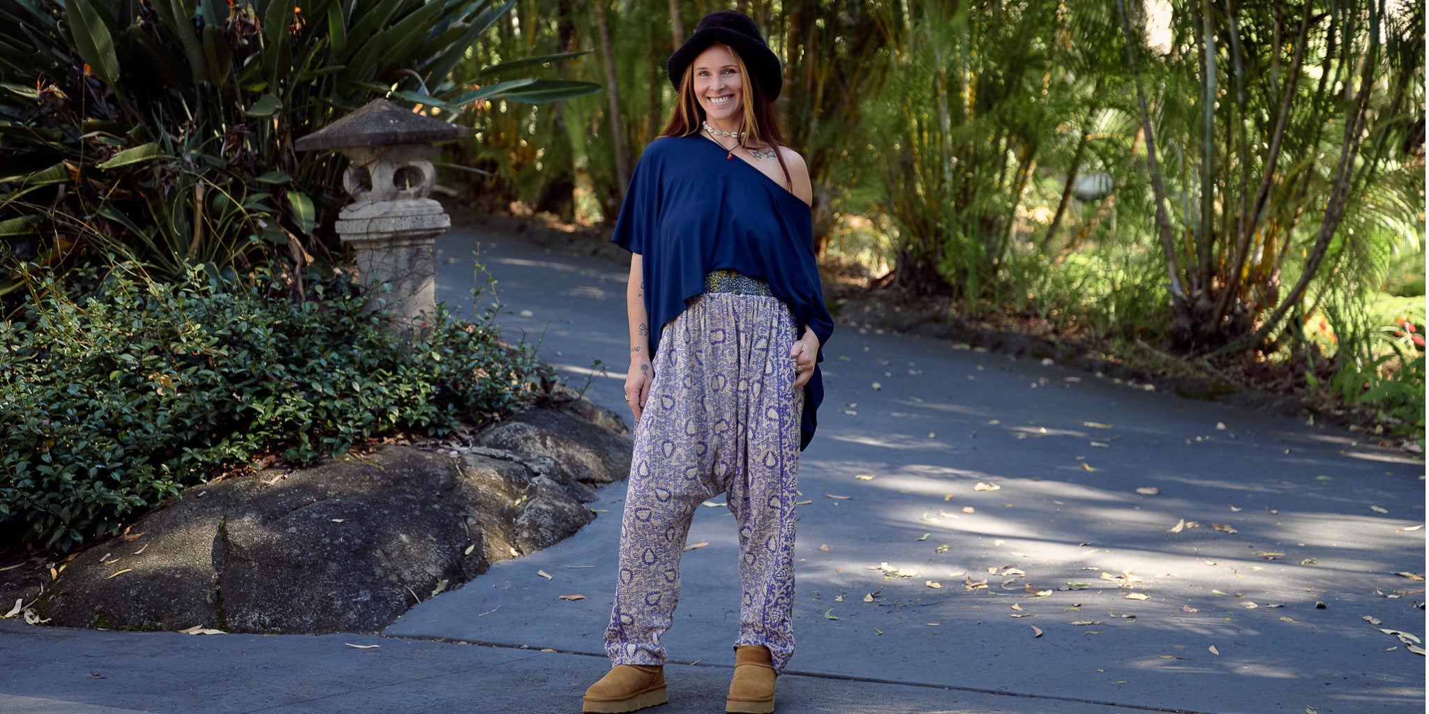 Woman in a garden wearing a blue top and harem pants.