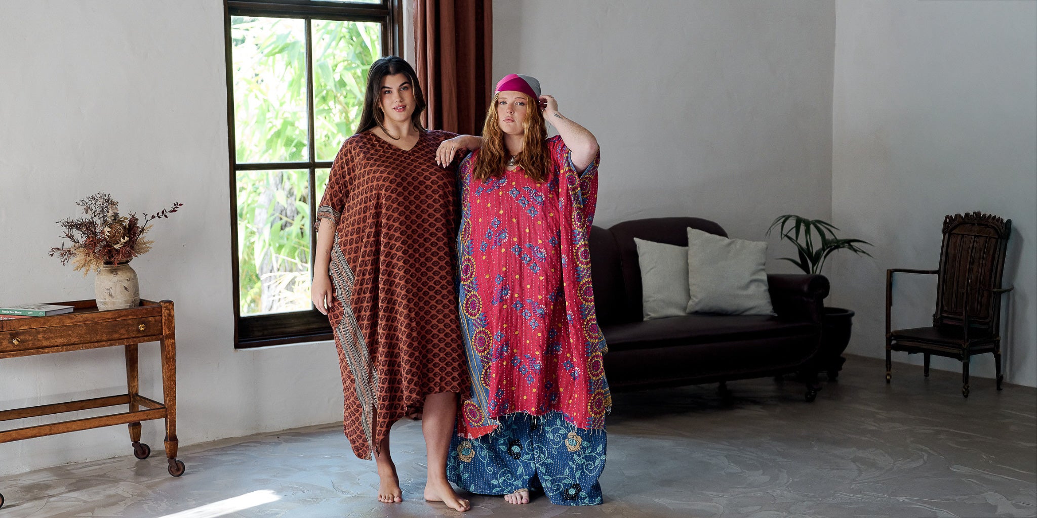 Two women standing in a living room wearing patterned dresses.