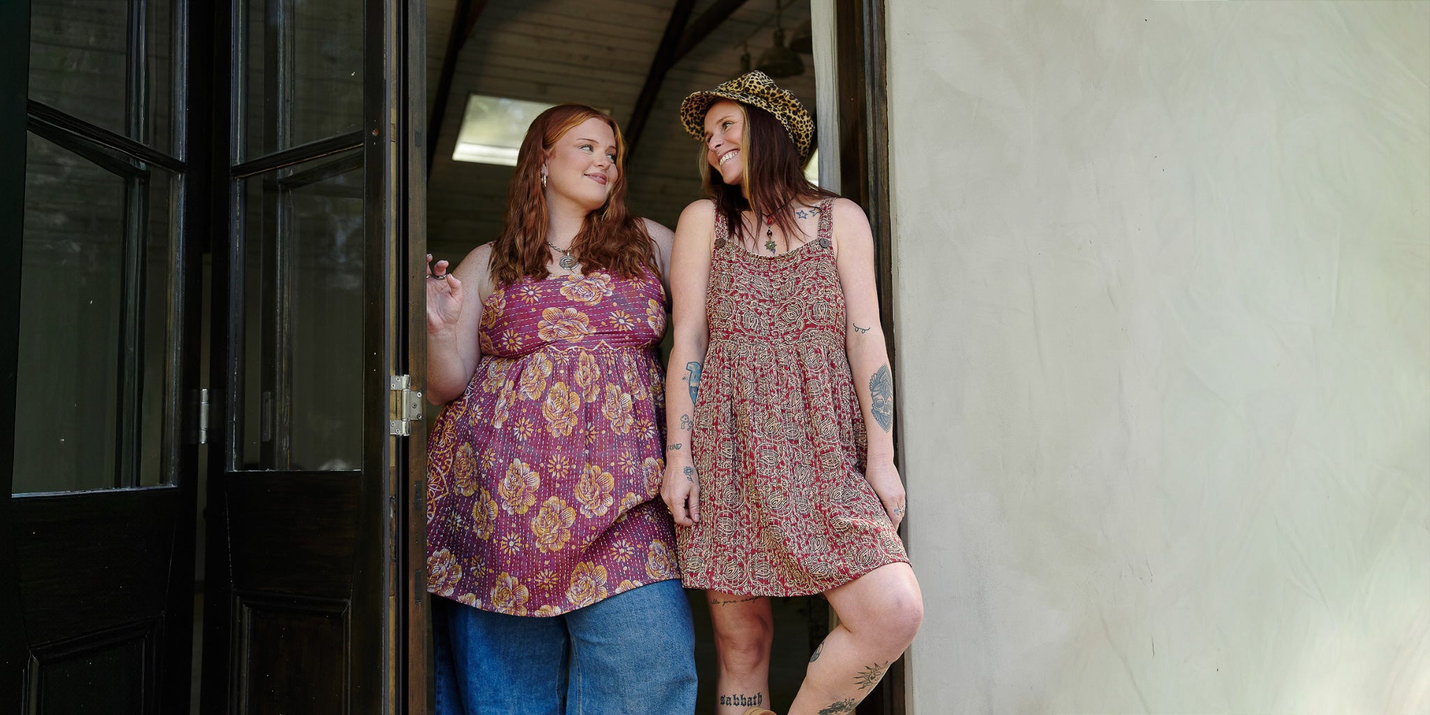 Two women standing in a doorway, wearing patterned dresses.