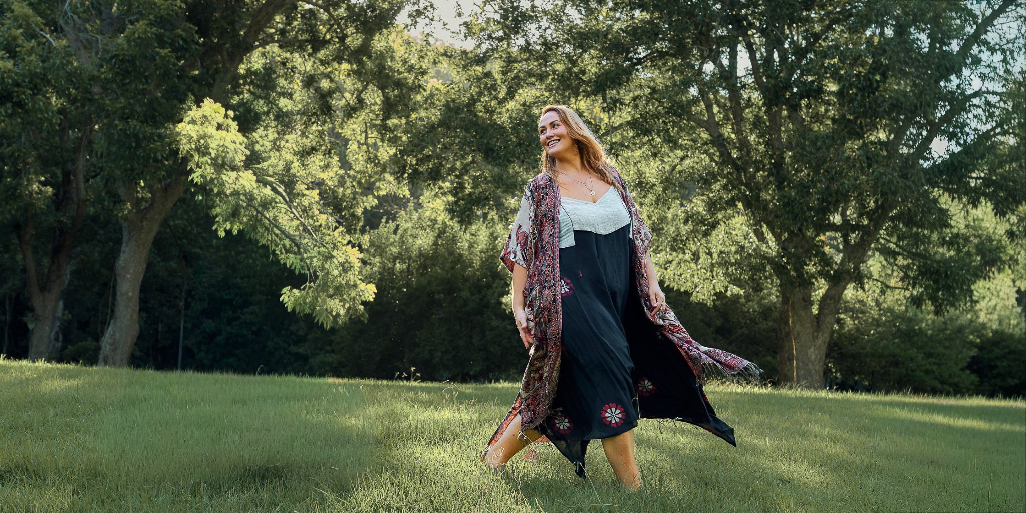 Woman in a long floral dress standing in a grassy field with trees in the background