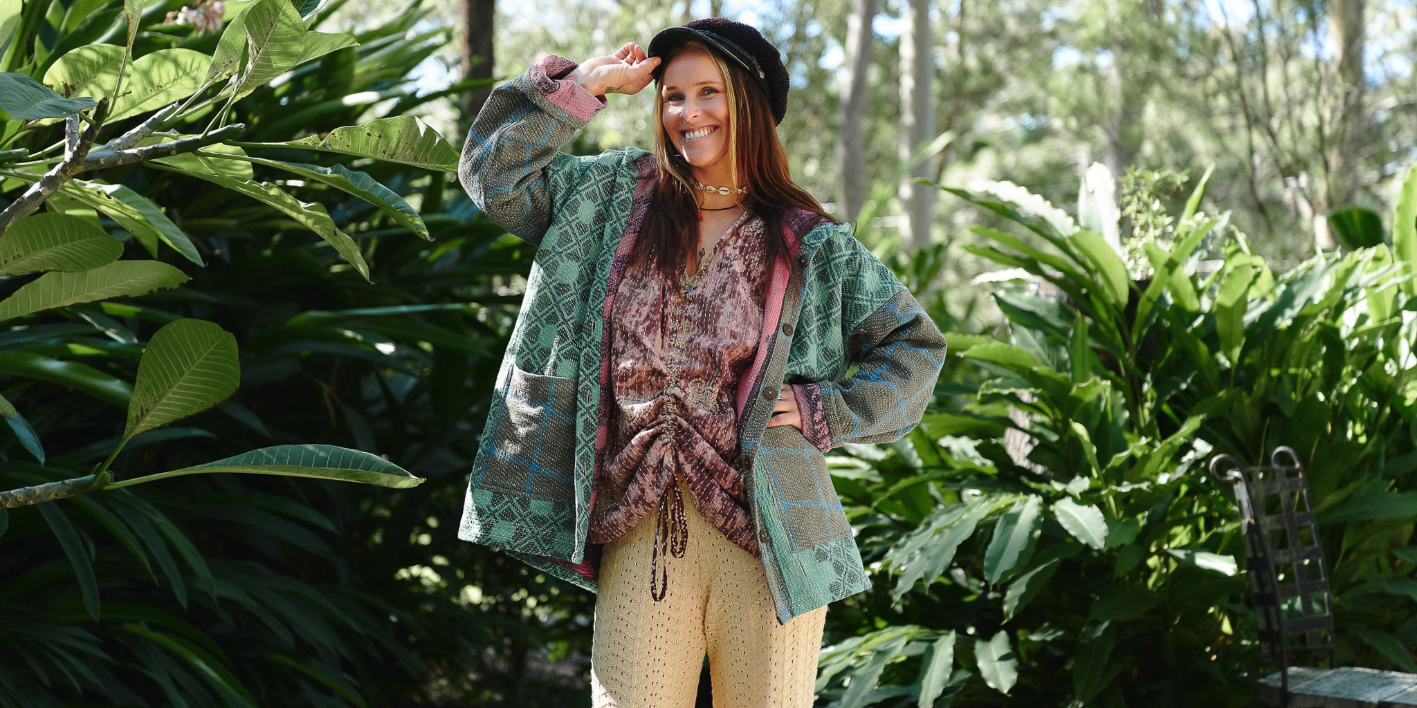 Woman in a patterned jacket and beige pants standing in a garden