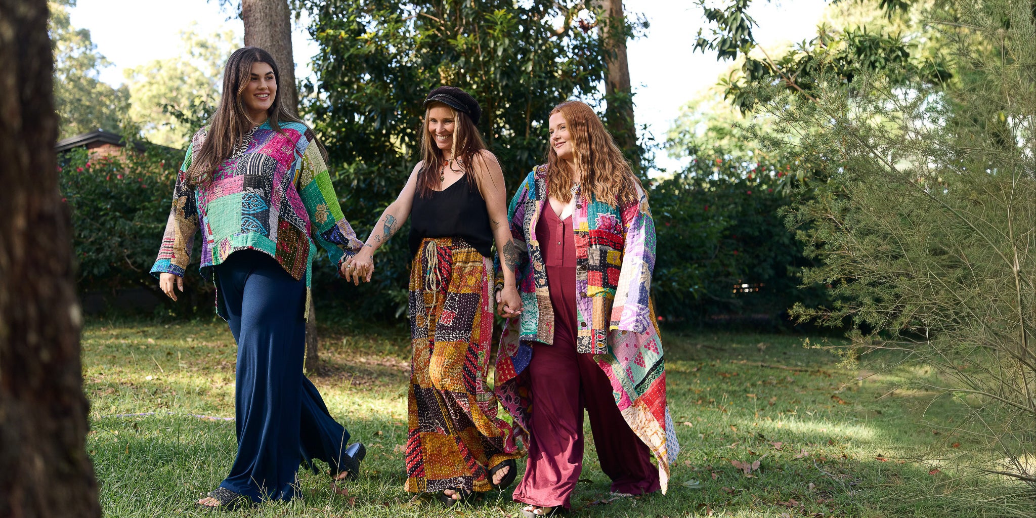 Three women holding hands in a park, wearing colorful clothing.
