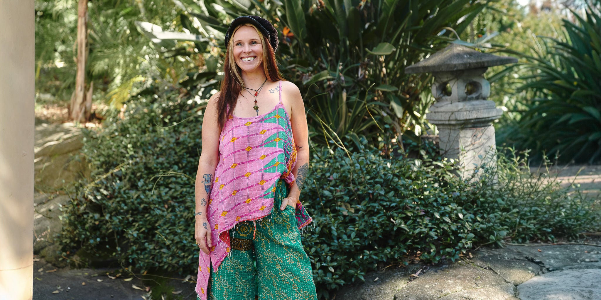 Woman in a colorful dress standing in a garden with greenery and a stone lantern in the background.