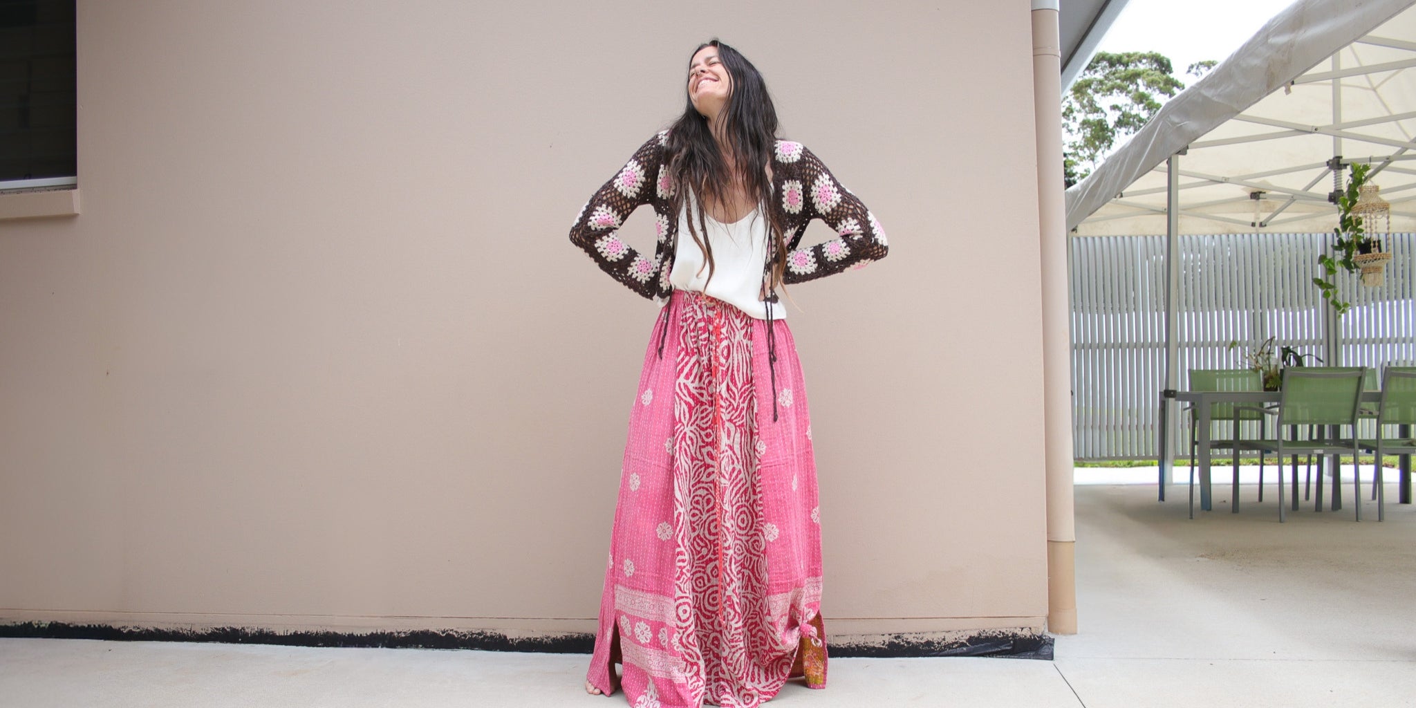 Woman in a pink patterned skirt and black jacket standing in front of a beige wall.