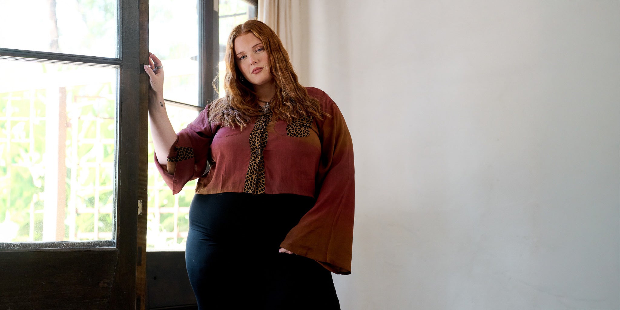 Woman wearing a patterned blouse standing in a room with a window.