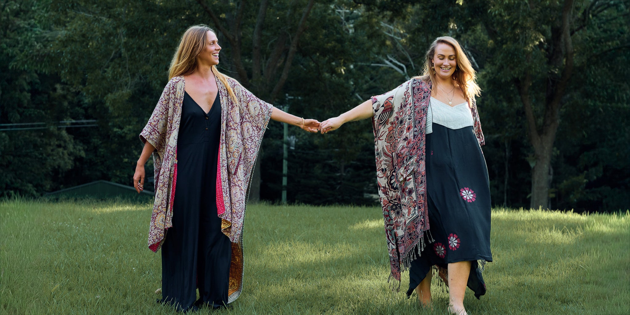 Two women holding hands outdoors in a grassy area with trees in the background