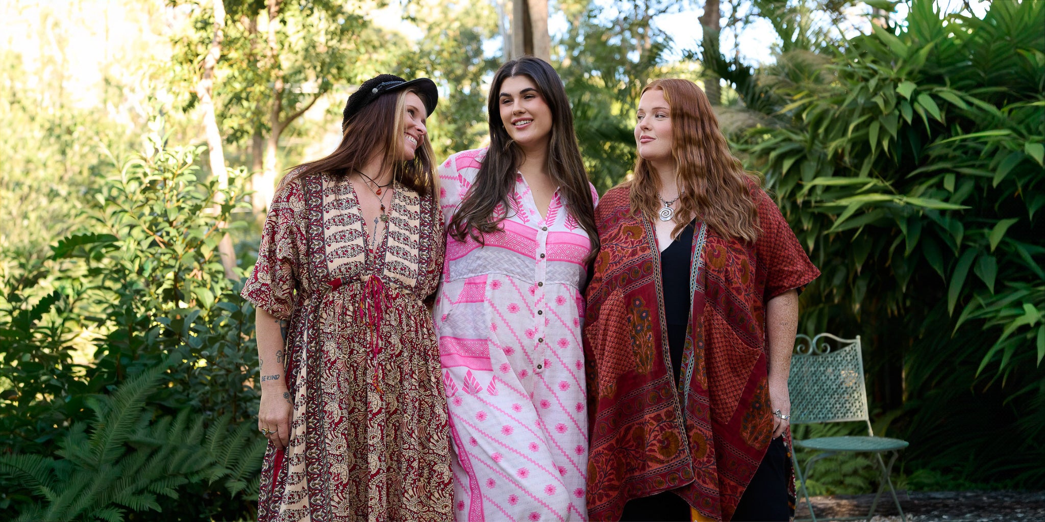 Three women standing together outdoors with greenery in the background