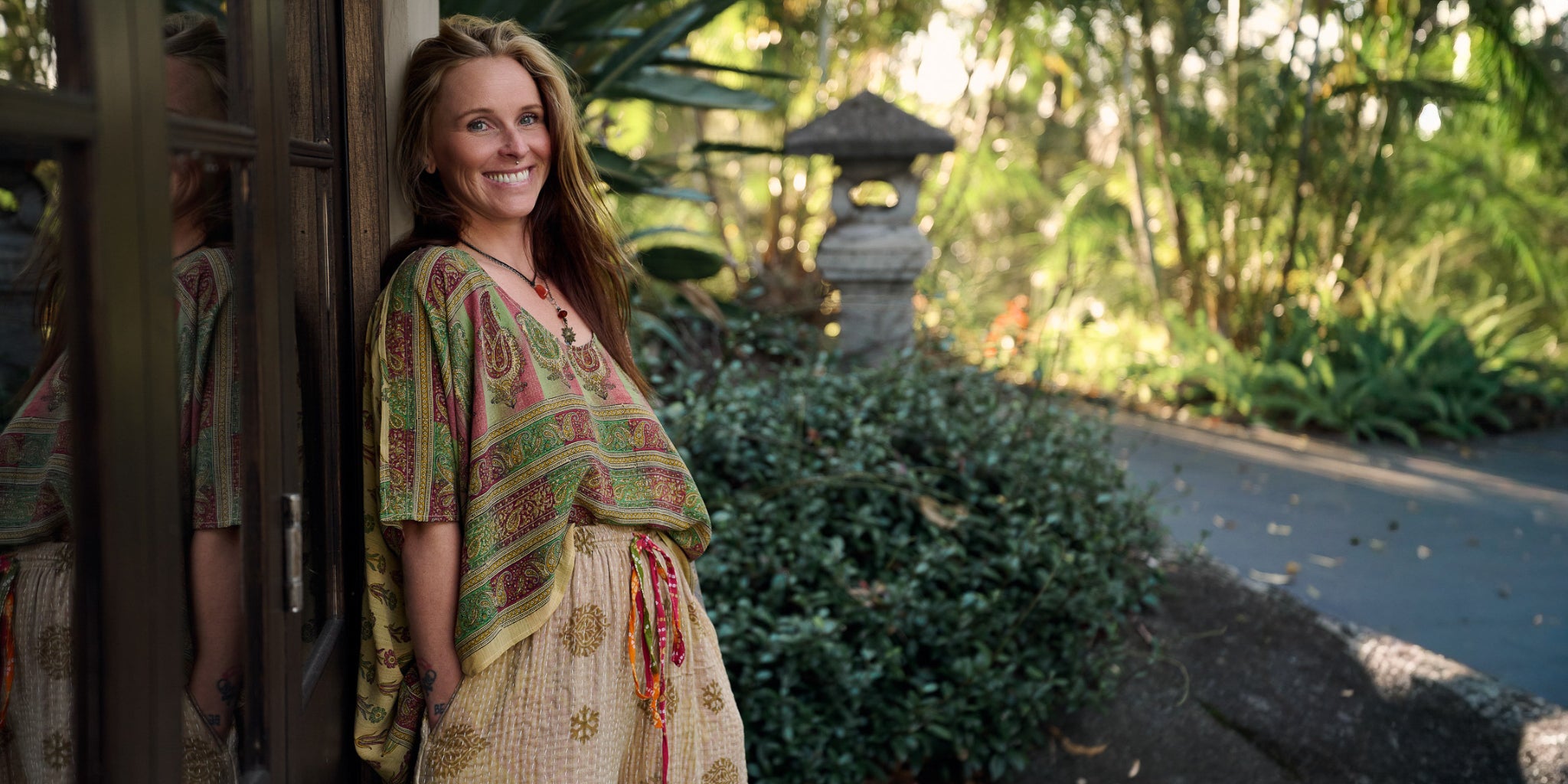 Woman in a recycled silk top standing in a garden with greenery and a path.