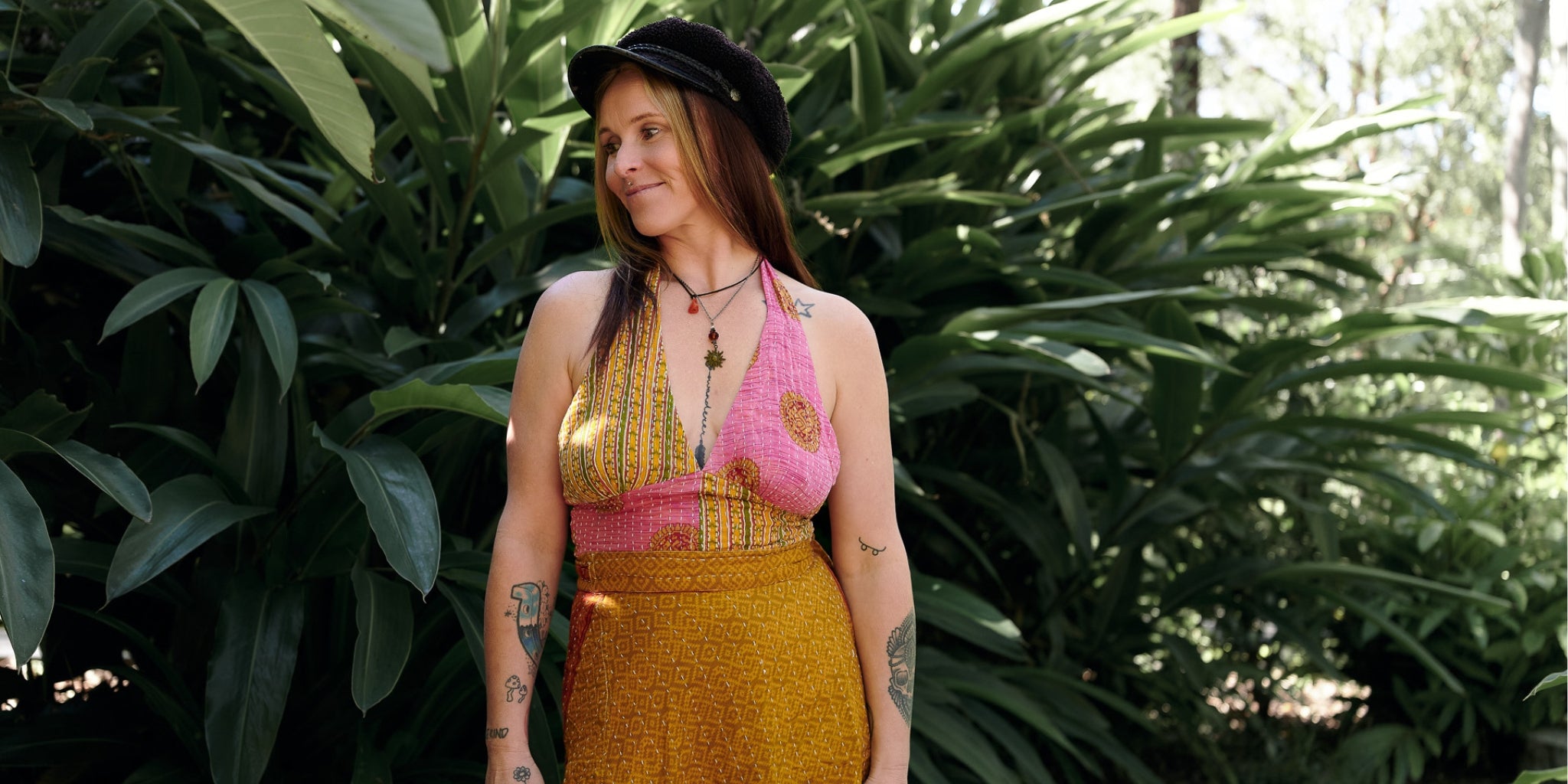 Woman in a yellow top and black hat standing among green plants