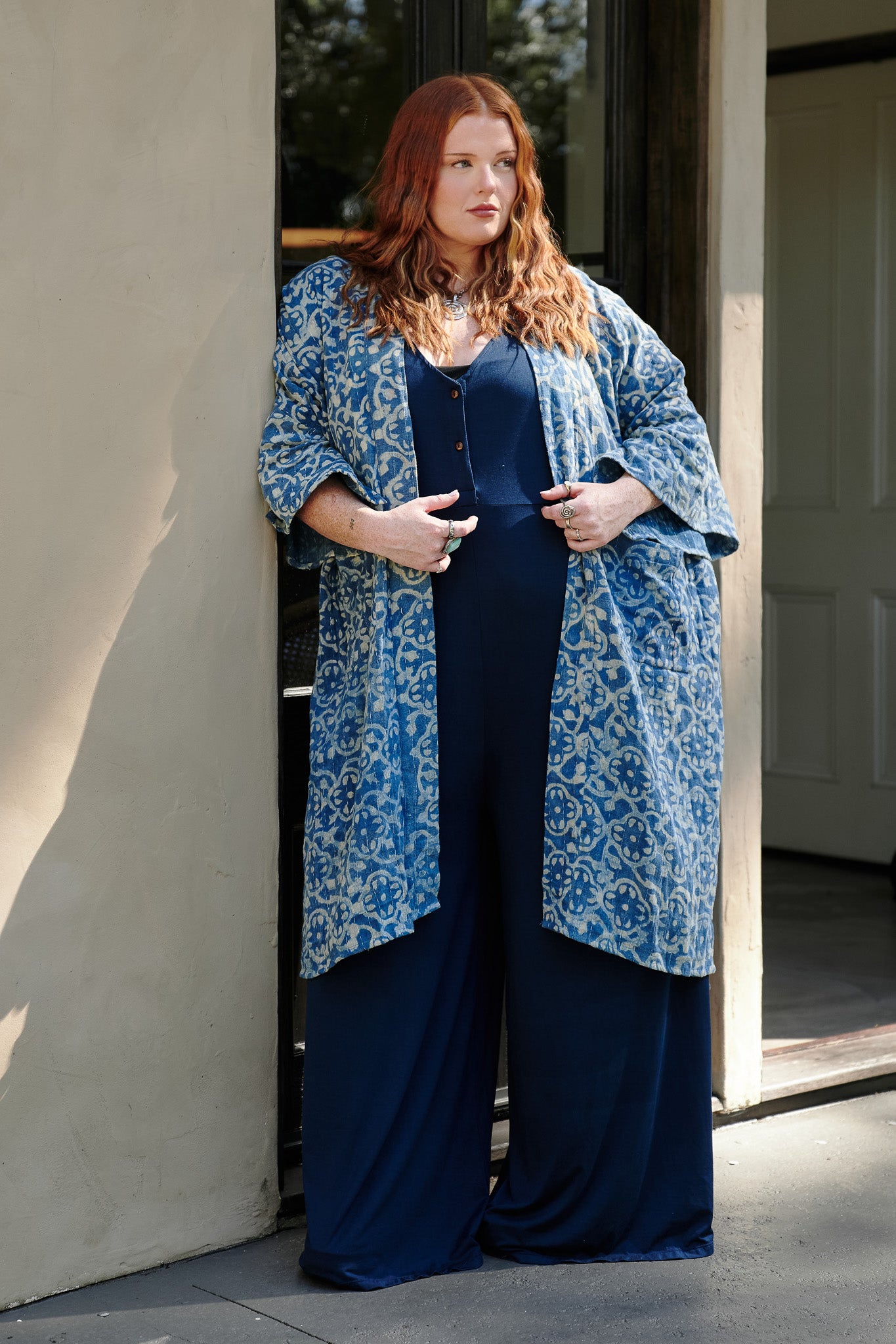 Woman wearing a blue patterned coat over a navy outfit standing in a doorway.