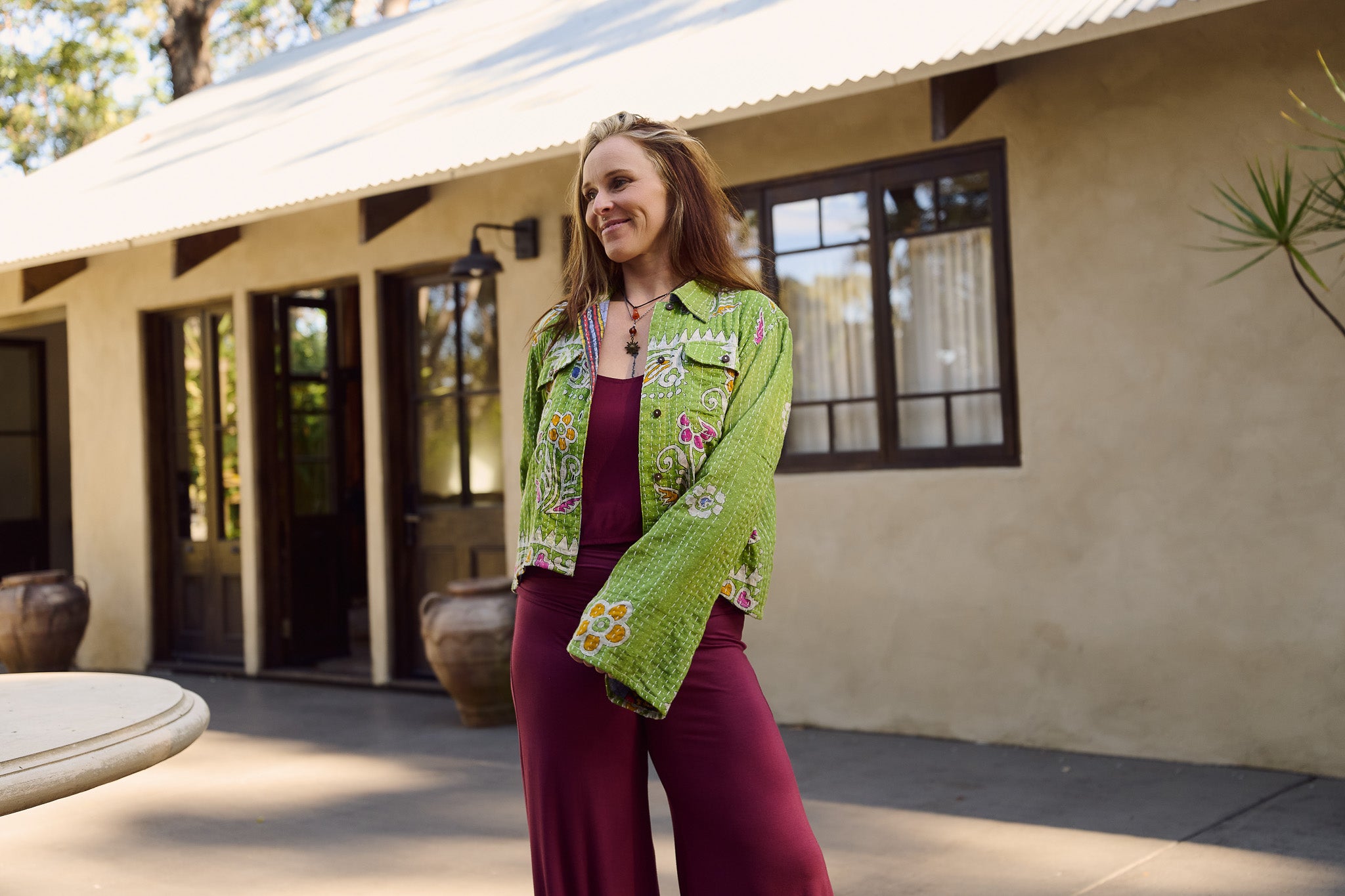 Woman wearing a green floral jacket and purple pants standing in front of a building.