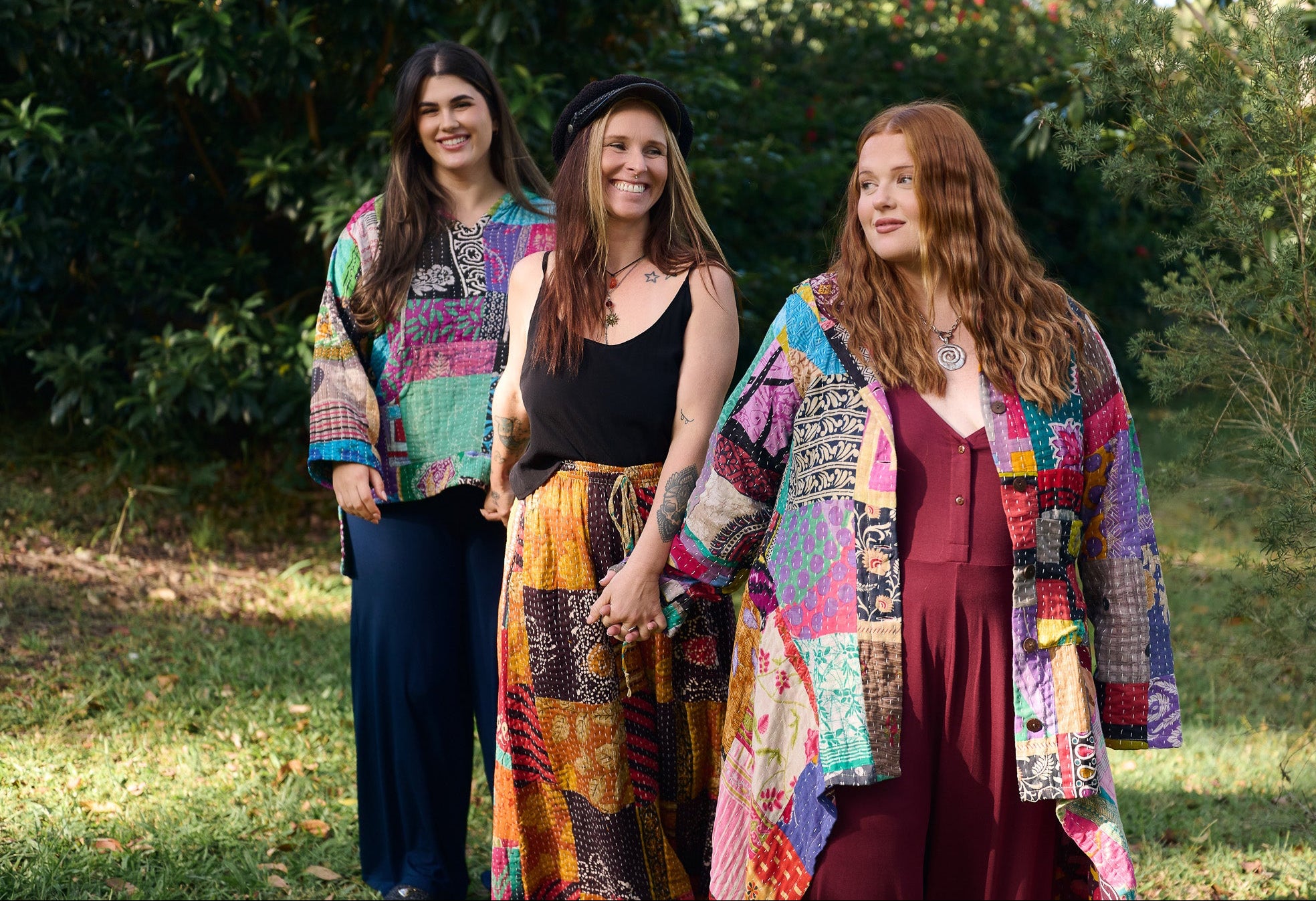 Three women wearing colorful patchwork clothing standing outdoors.