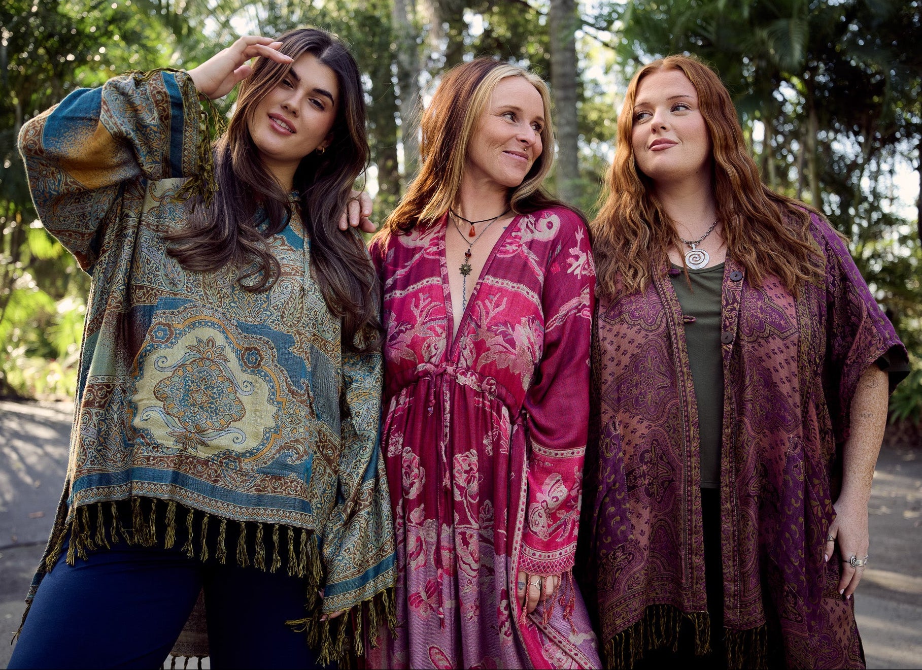 Three women wearing patterned cardigans standing outdoors with trees in the background