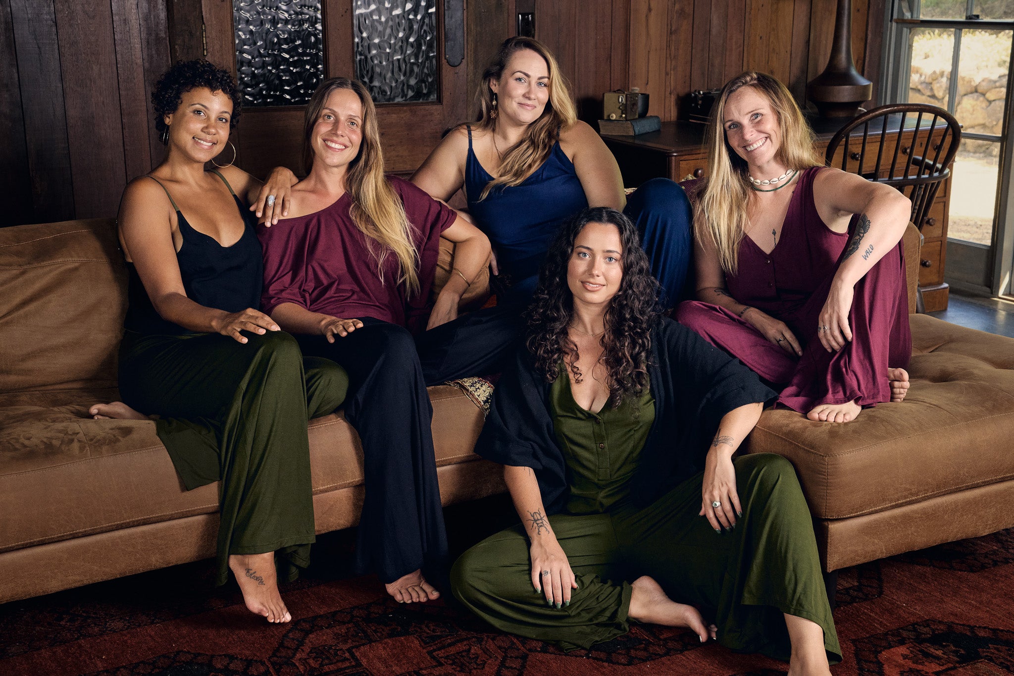 Five women sitting on a couch in a warm, indoor setting.