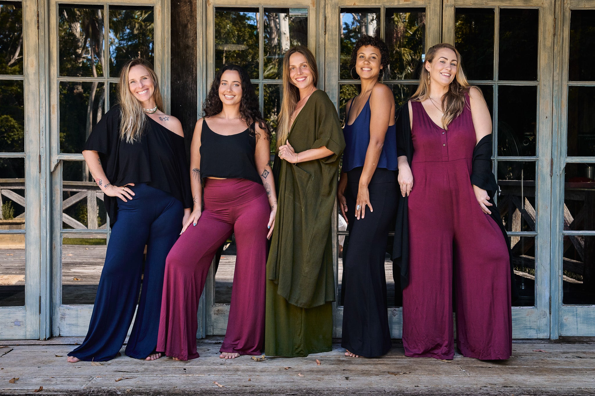 Five women posing together on a wooden deck with a rustic building in the background.