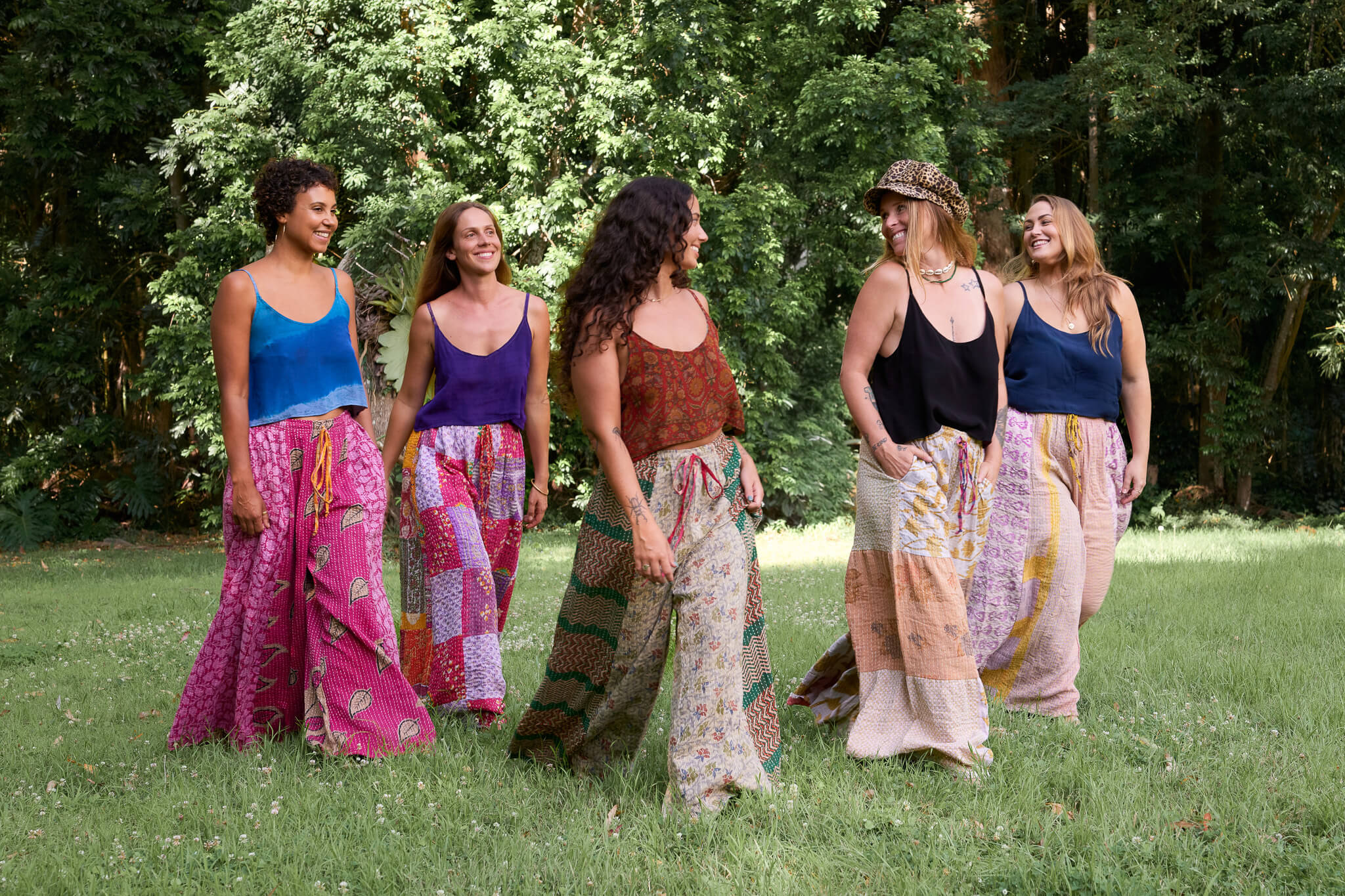 Five women in colorful outfits standing in a grassy area with trees in the background