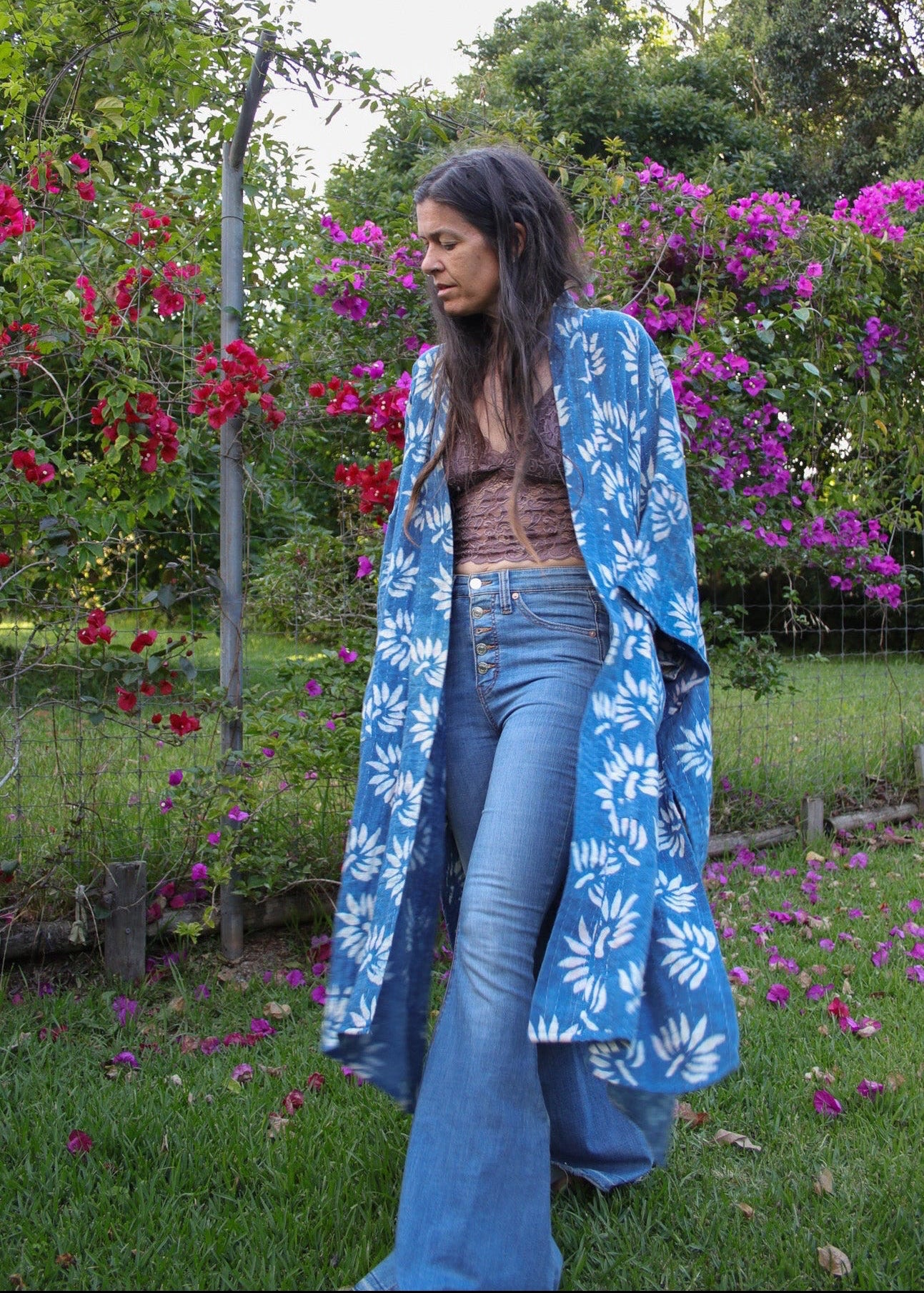Woman wearing a blue floral kimono in a garden with flowers and greenery.