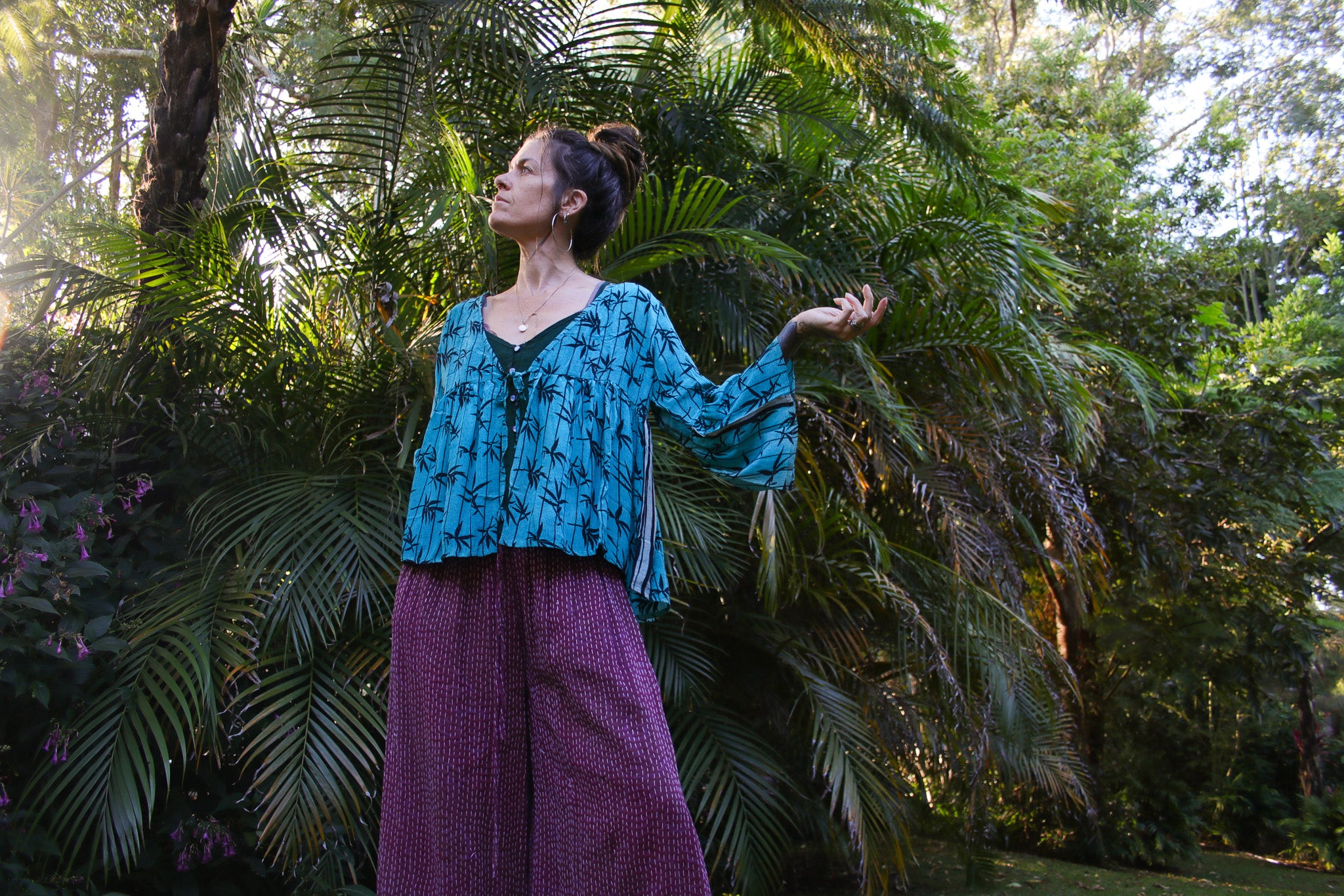 Woman in a blue top and purple pants standing among tropical plants