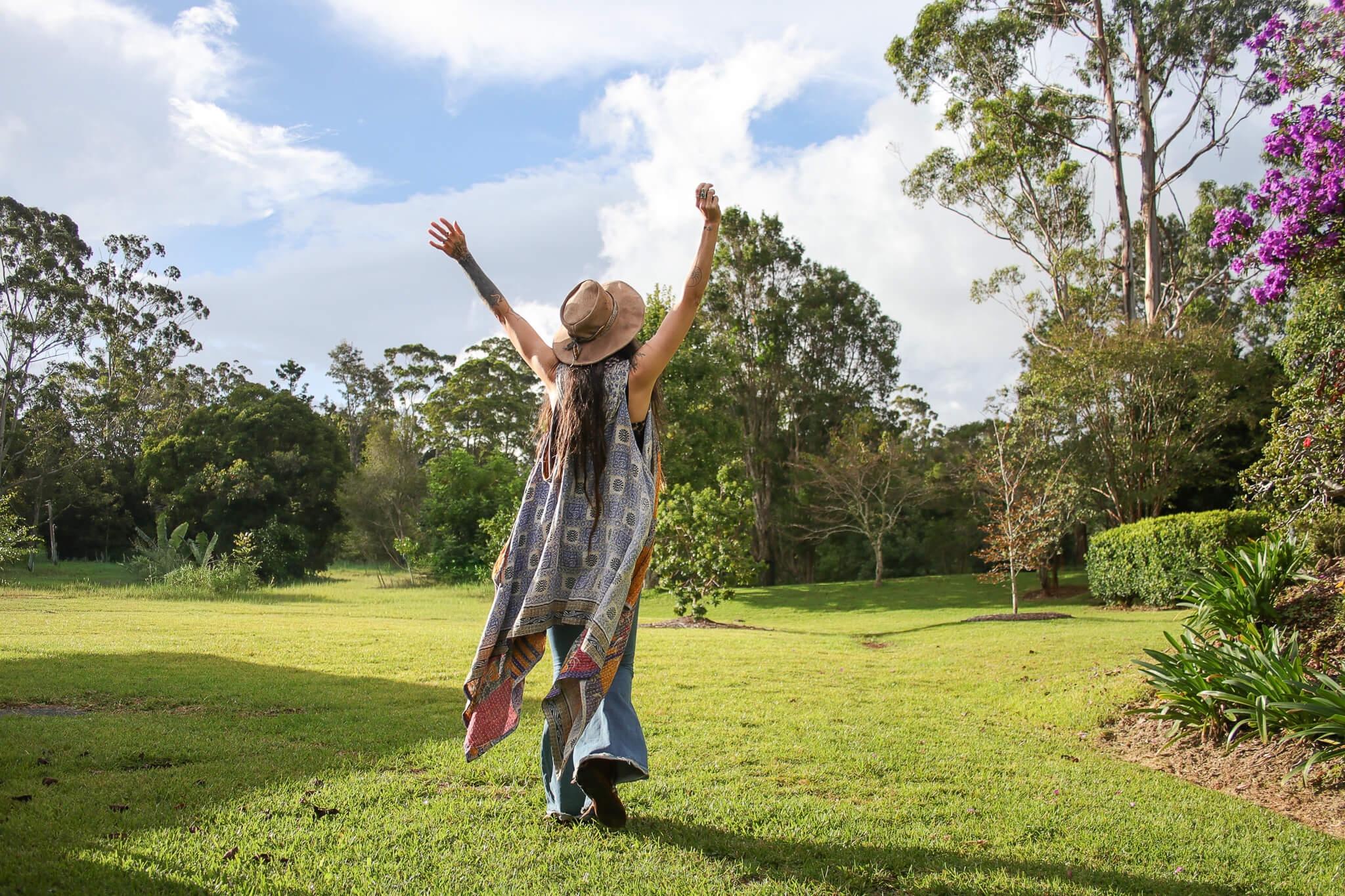 Person with arms raised in a park with trees and flowers