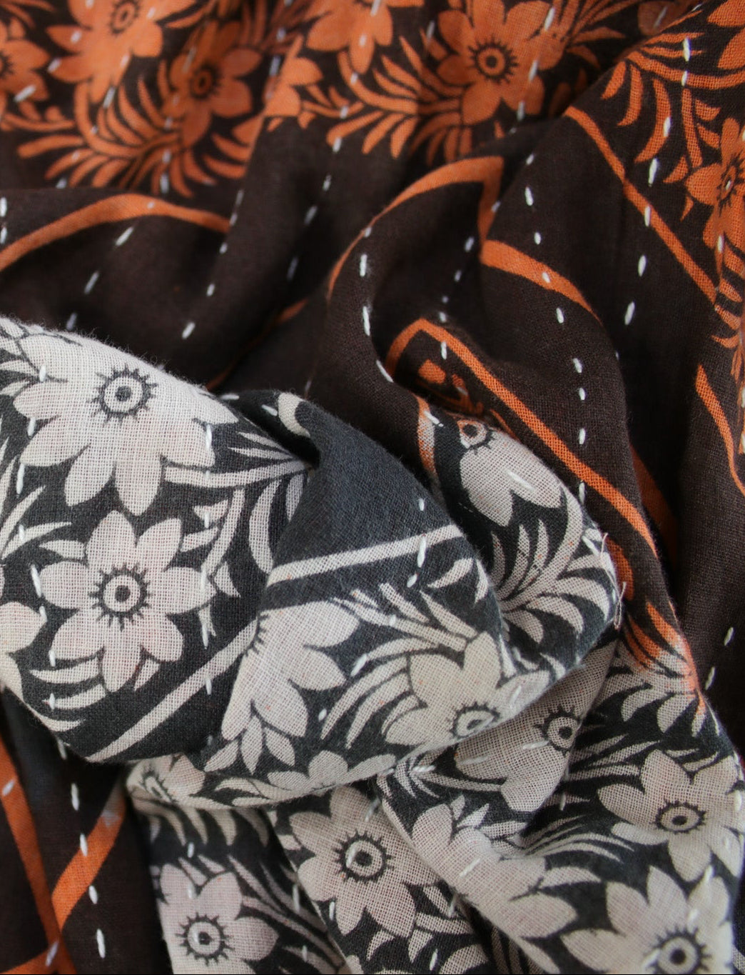 Close-up of patterned fabric with floral and geometric designs in black, white, and orange.