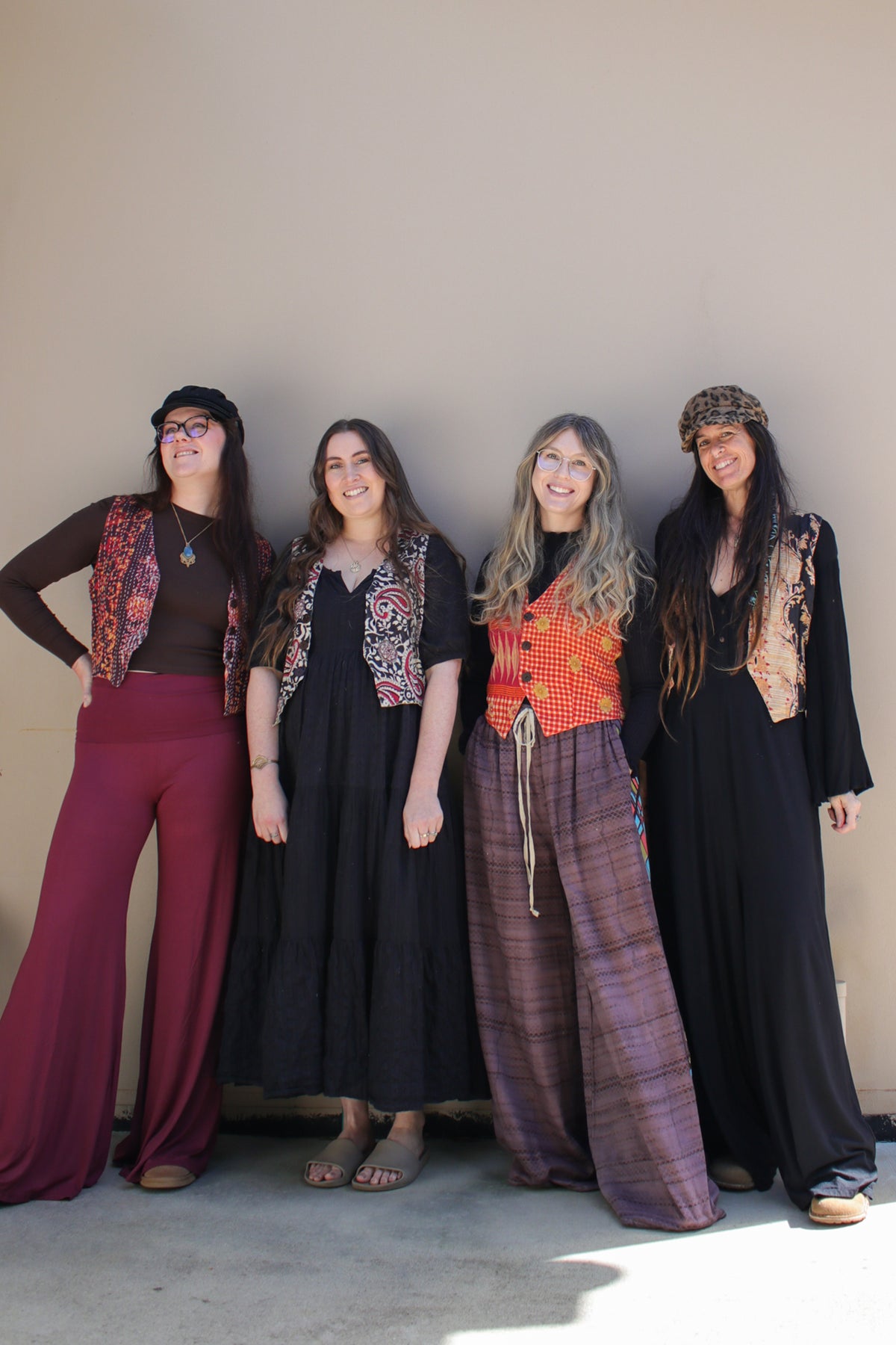 Four women standing side-by-side in bohemian-style clothing against a plain beige wall.