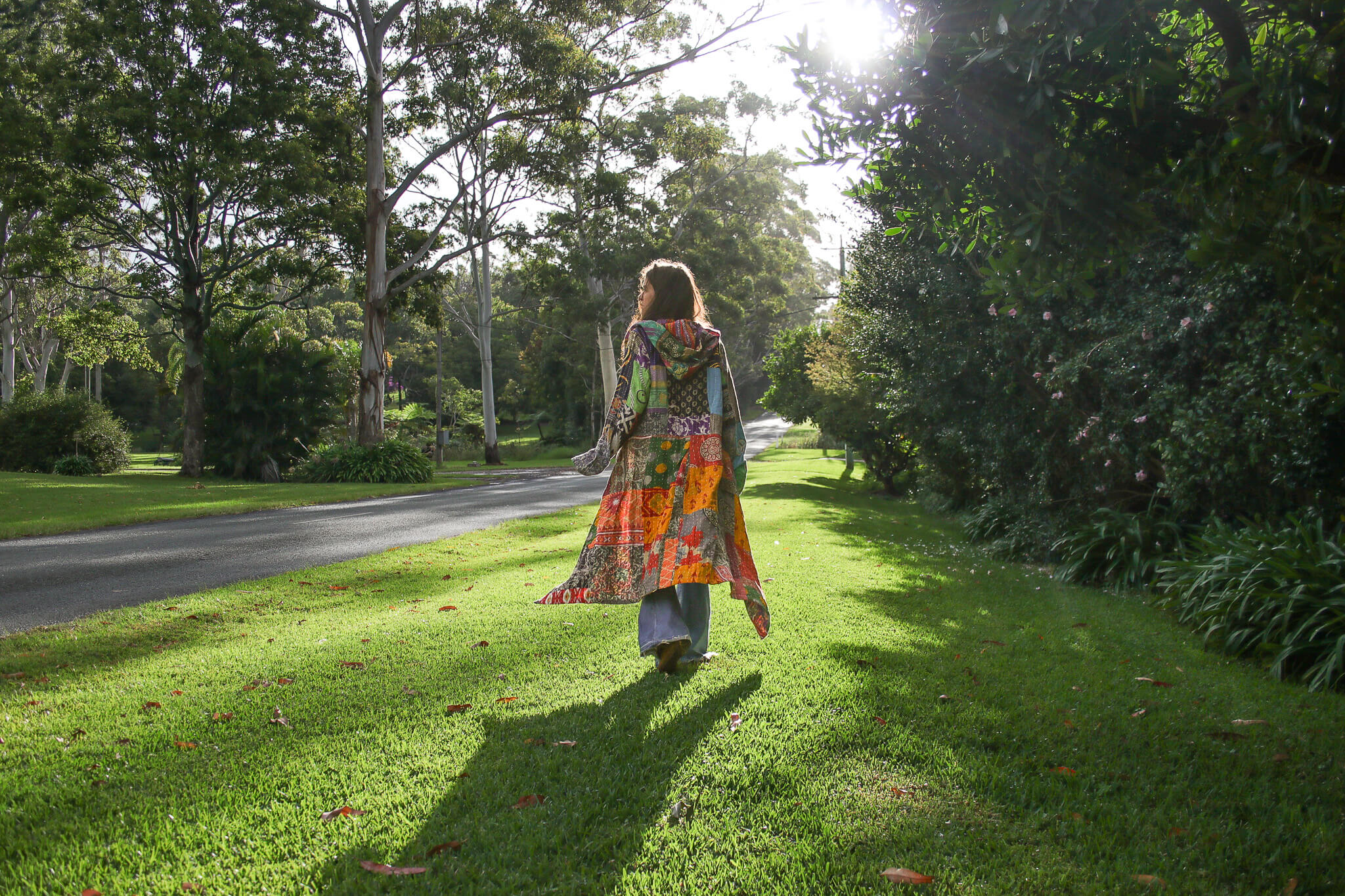 Woman in a colorful dress walking on a grassy path in a park in a patchwork coat